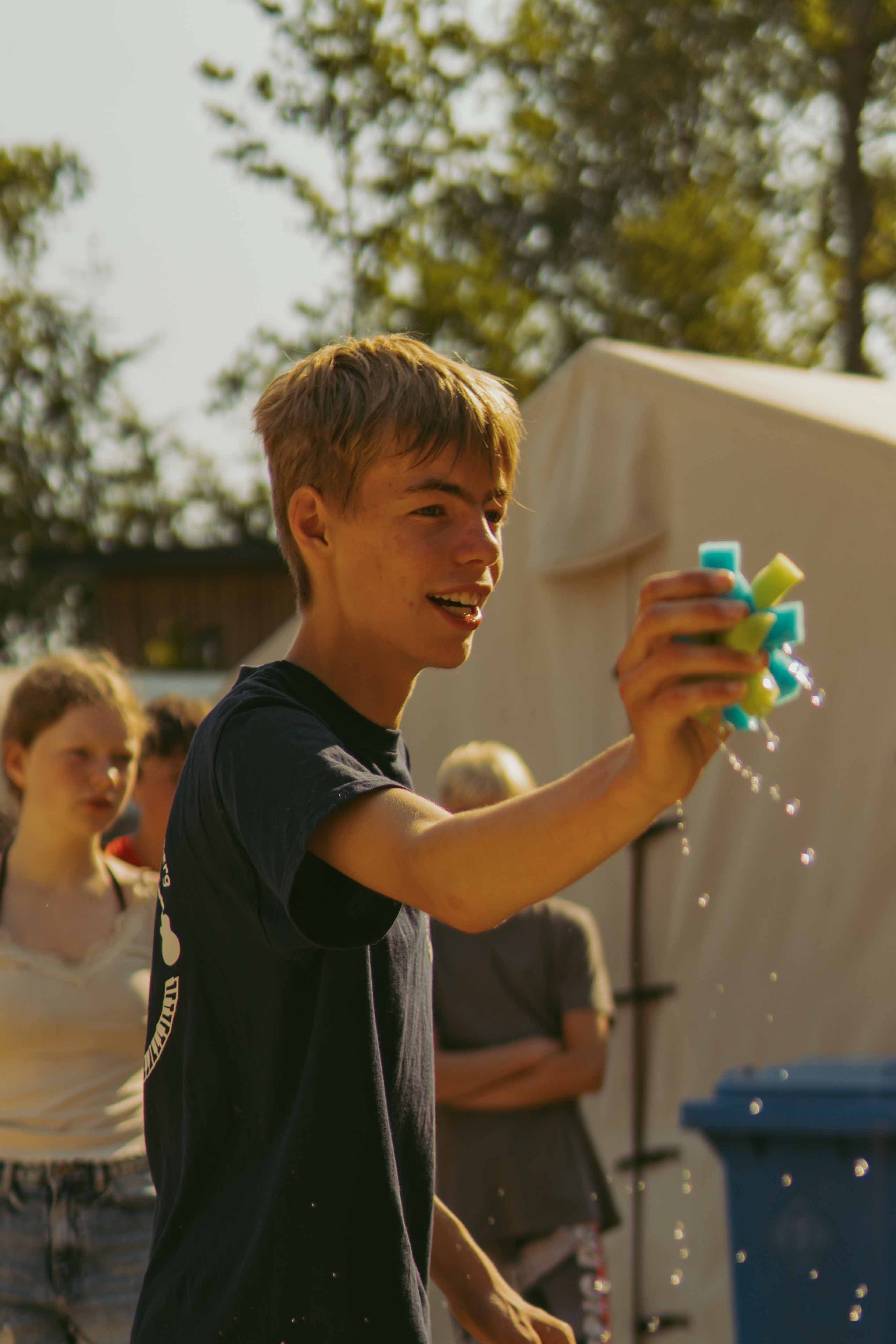Jugendlicher lacht beim Spielen mit Wasserspielzeug im Freien